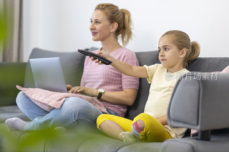 快乐的女人在用笔记本电脑，女儿在用电视遥控器