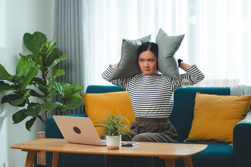 亚洲女人觉得无聊，有噪音遮住耳朵和枕头坐在家里的问题。