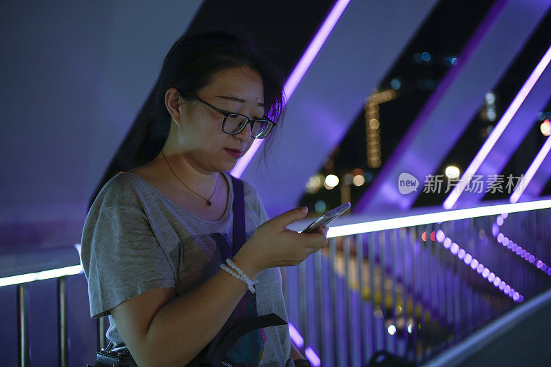 女子晚上在城市的人行天桥上使用智能手机