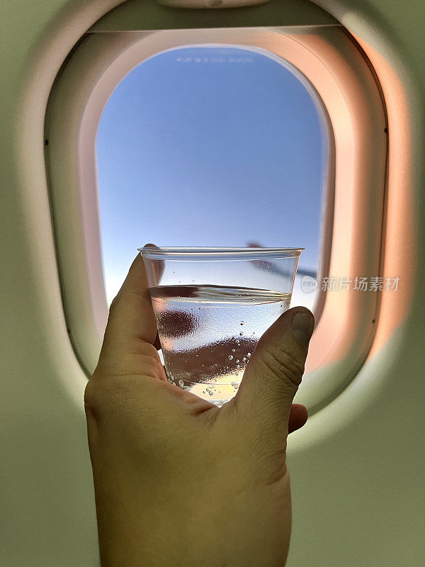 个人视角的舷窗，当一个拉丁裔的年轻人放松，喝着一杯苏打水坐在飞机的经济舱在飞行。