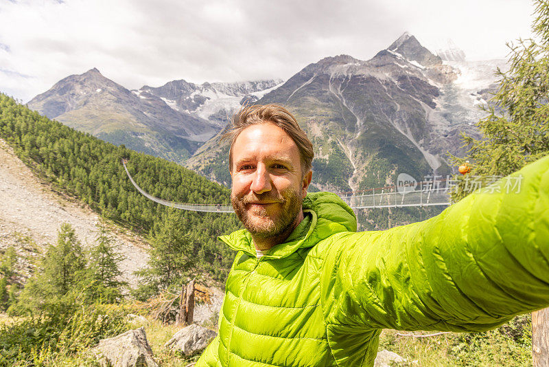 一名男子在阿尔卑斯山徒步旅行，以吊桥为背景自拍