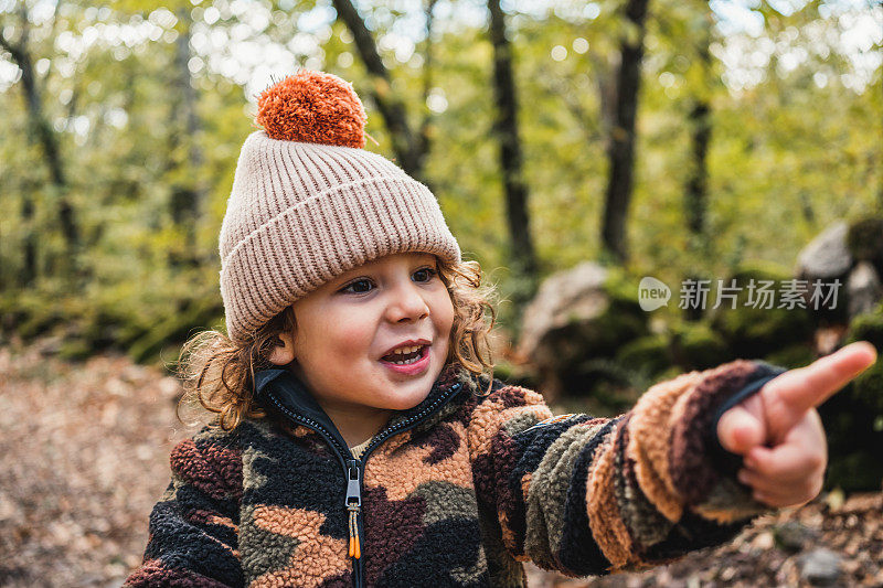 一个漂亮时髦的小男孩戴着帽子在森林里指着前方