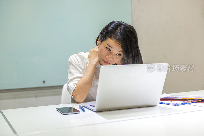 一个亚洲女人在他的办公桌上拿着文件和笔记本电脑工作