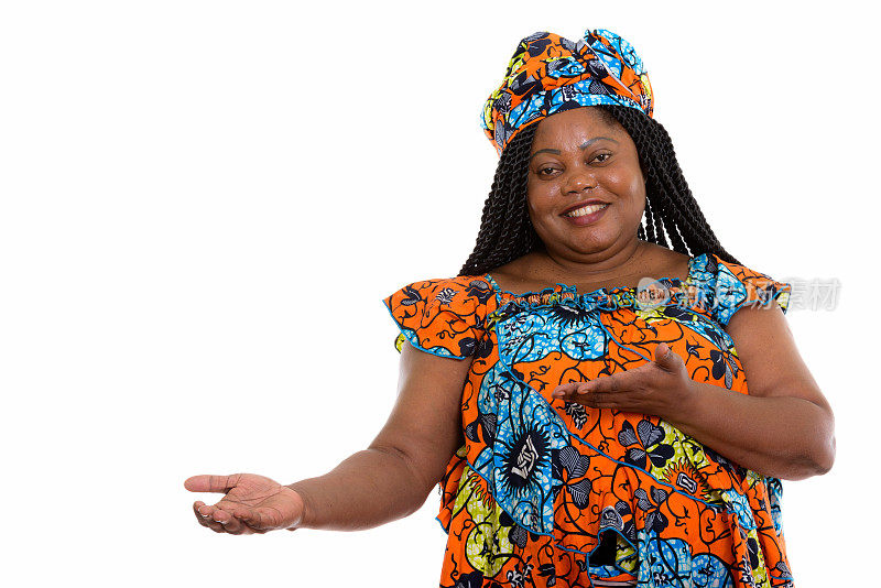 工作室拍摄的快乐的大码非洲黑人妇女微笑着，穿着传统服装展示一些东西