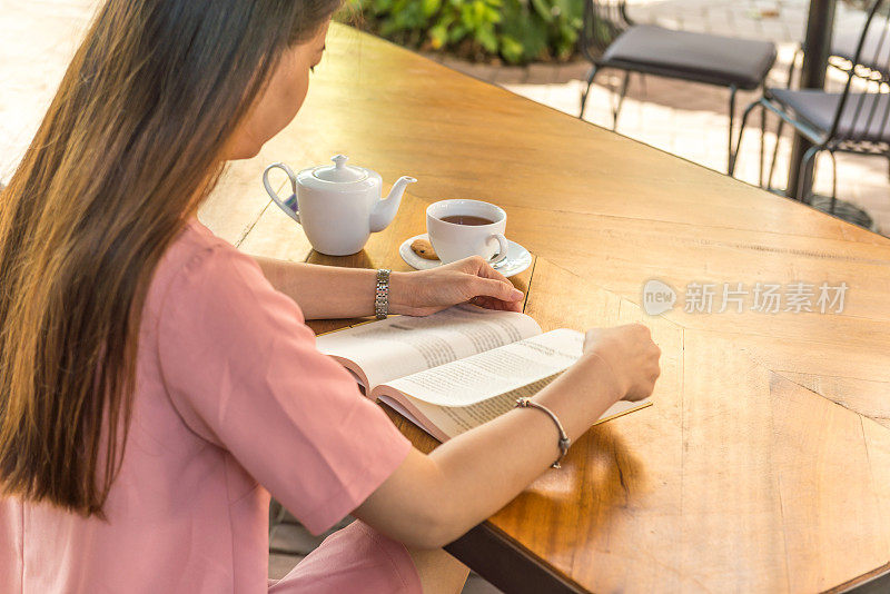 后视图的年轻女子看书与一杯热茶旁边
