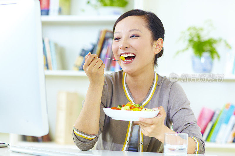 年轻女子坐在电脑前享用沙拉