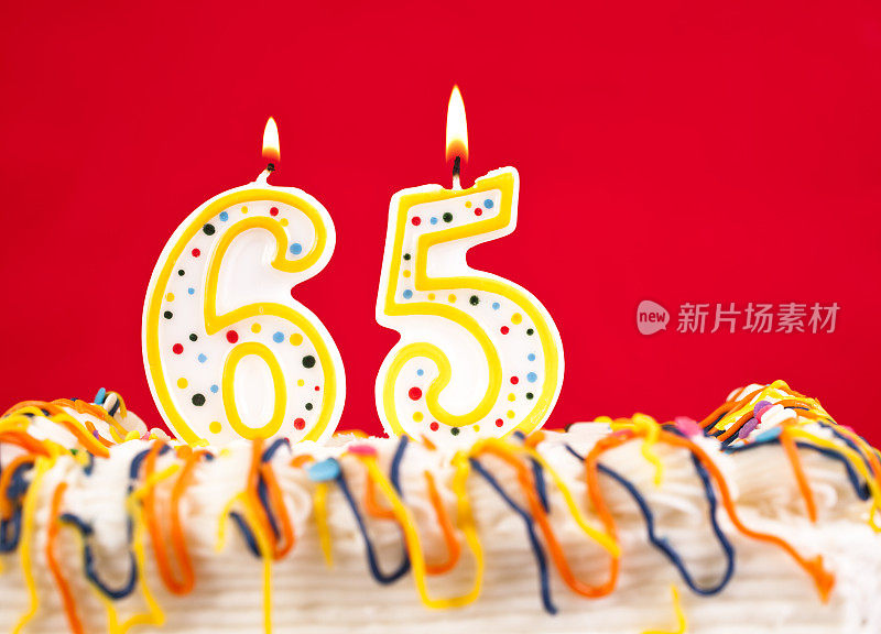 用65号燃烧的蜡烛装饰生日蛋糕。红色的背景。