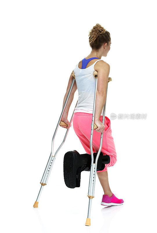 受伤妇女拄着拐杖走路的后视图