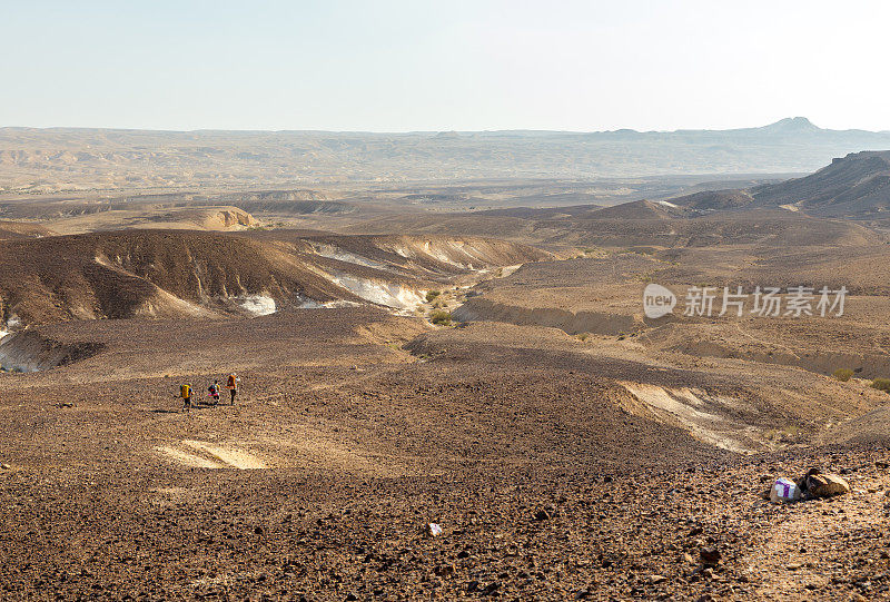 三个背包客走在石头沙漠小径上。