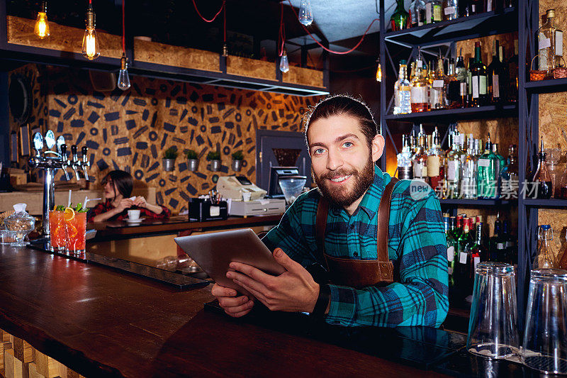 带着平板电脑的咖啡师在酒吧的工作场所微笑
