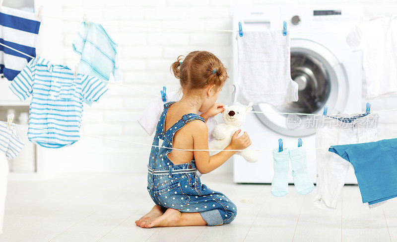 孩子有趣的小女孩洗衣服和泰迪熊在洗衣房