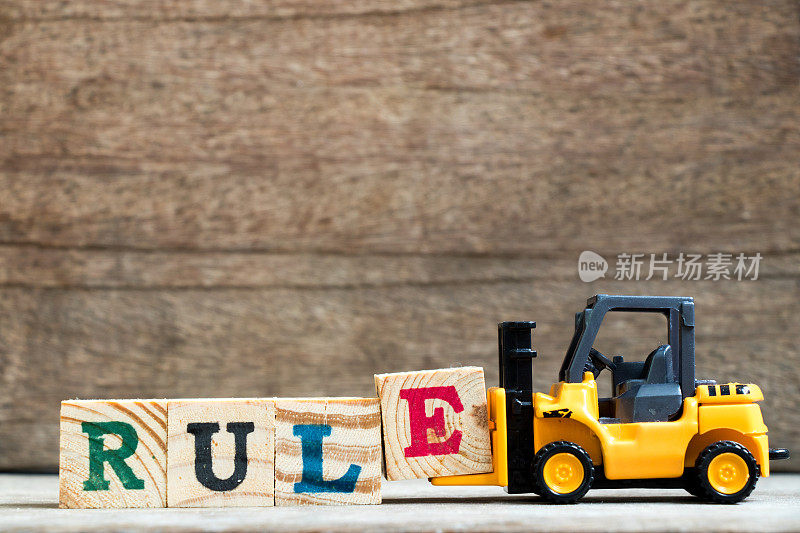 黄色塑料玩具叉车托起字母块E来完成单词规则在木头背景上