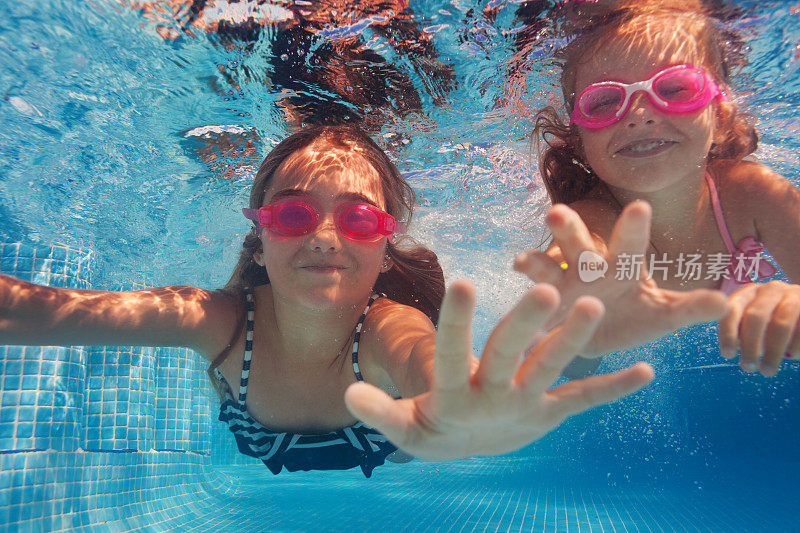 两个快乐的女孩戴着护目镜在水下游泳