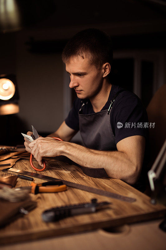皮带在皮革车间的工作过程。手持制作工具的人正在工作。旧制革厂的皮匠。木桌上的背景。靠近男人的手臂