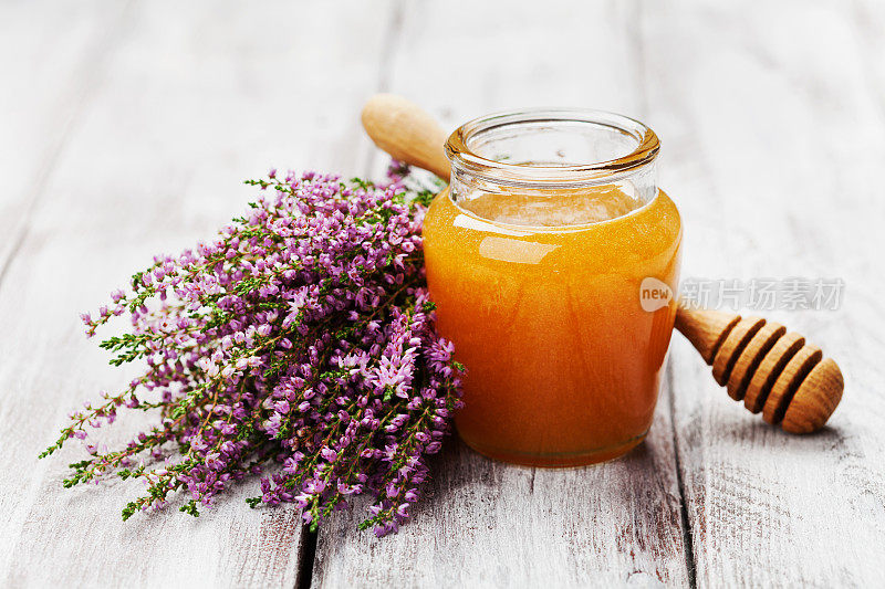 美味的新鲜蜂蜜在罐子或罐子和花石南在木制的复古背景。
