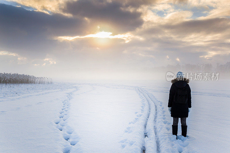 在晴朗多云的冬日下午，女人在雪湖上的薄雾中。在宁静的气氛中独自漫步。多雾的空气。自然概念中的美丽时刻。