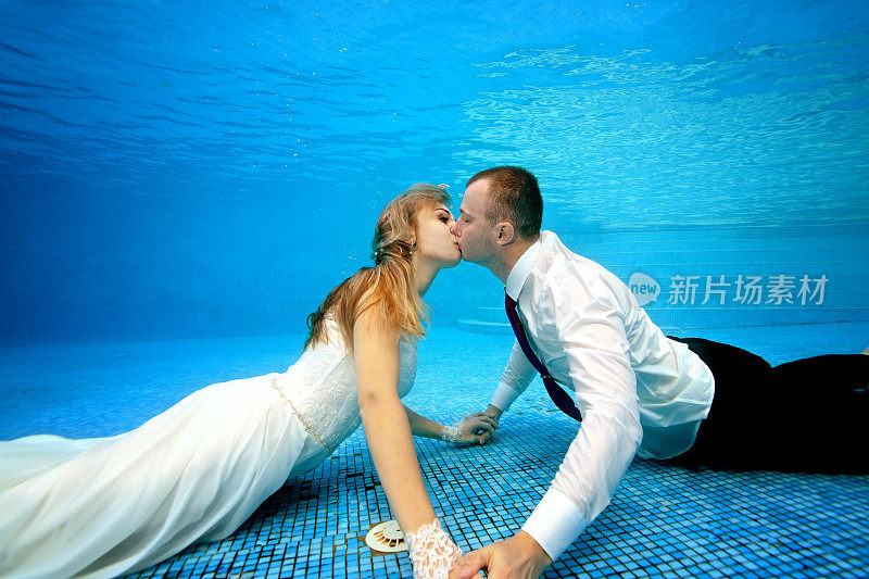 快乐的新娘和新郎穿着婚纱在池底亲吻。肖像。在水下拍摄。横向