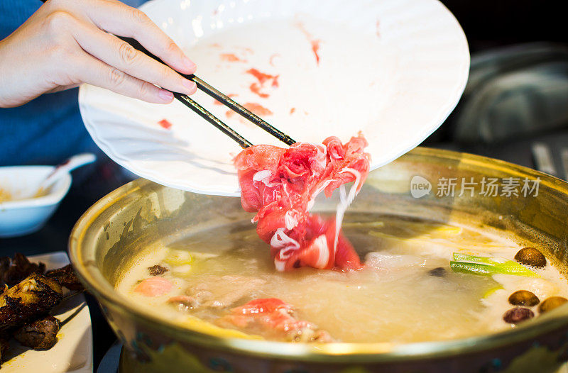 用筷子将羊肉片插入火锅中