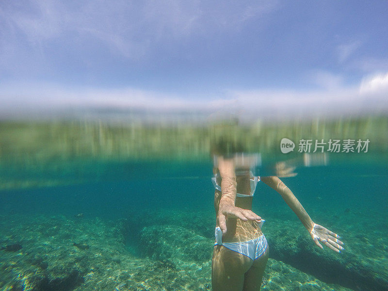 水下拍摄的年轻女子站在热带清澈的海水中度假的人的概念