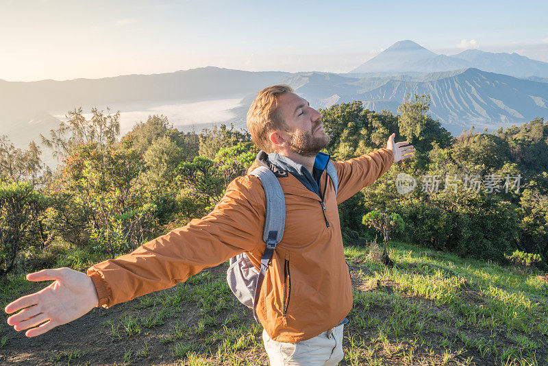 在印度尼西亚，年轻人徒步旅行，手臂伸开站在火山的山顶上，人们旅行的乐趣，冒险的概念，成功和成就