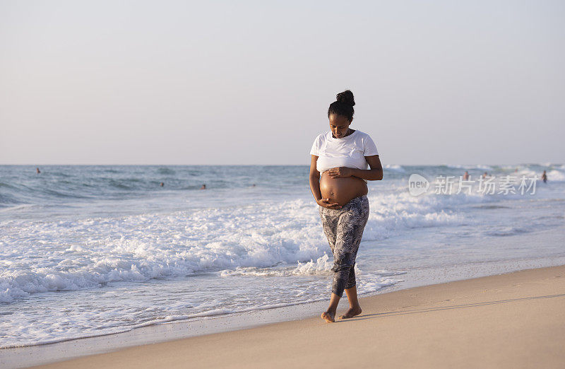 一名孕妇在日落时分沿着海滩散步。