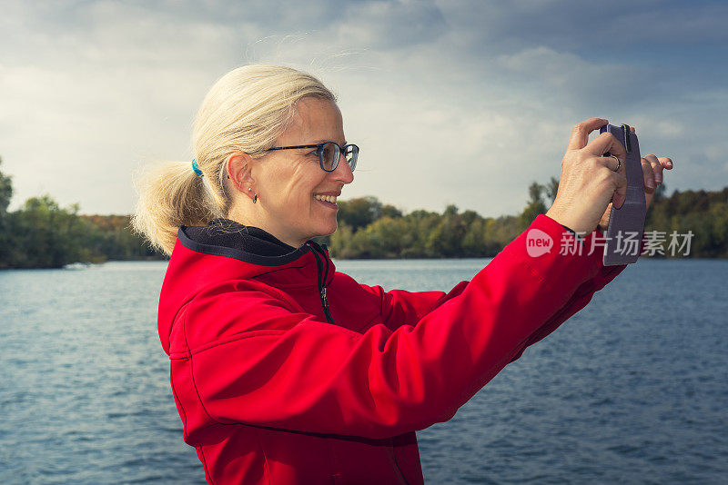 一个拿着数码相机在湖上自拍的女人