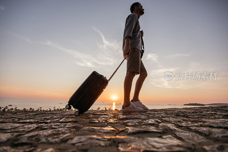 一个游客提着箱子在海边散步