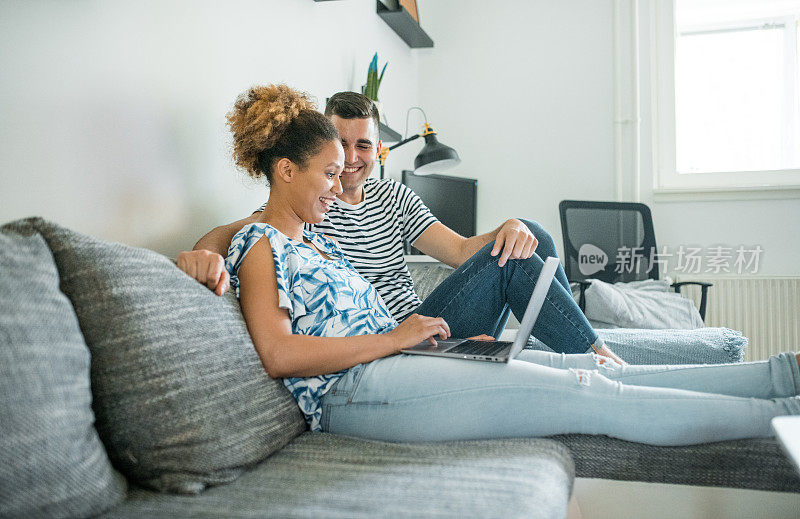 一对年轻夫妇坐在沙发上，用着笔记本电脑