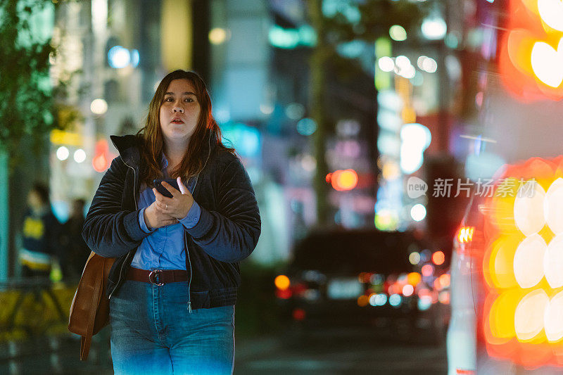 年轻女子拿着智能手机，晚上在城市里行走