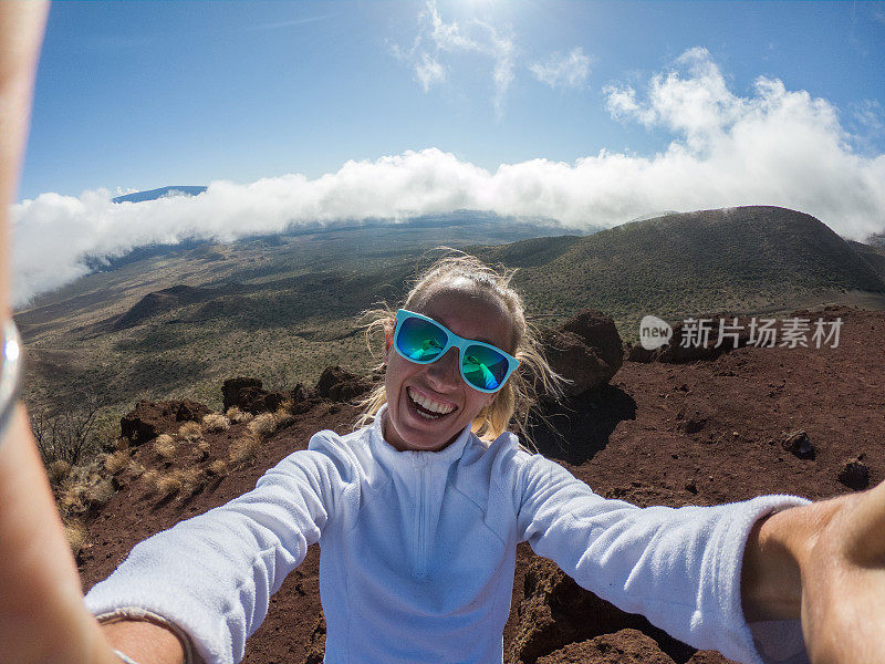 一名快乐的年轻女子在日落时火山上的云层上方自拍