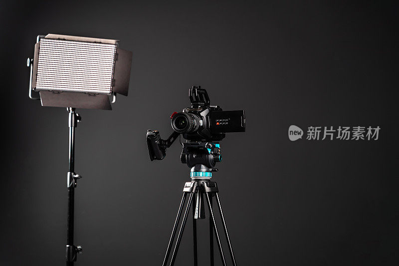 专业影院摄像机在一个摄像机三脚架和一个照明LED面板在黑色工作室背景