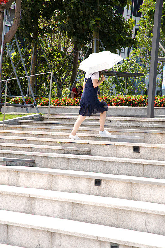 在中国深圳的深圳人才园，一位女士正在爬上台阶，打着伞躲避烈日。这个公共主题公园与深圳湾公园和湾体育馆相连