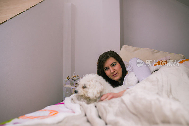 年轻女子在晚上躺在床上，享受着与她可爱的小狗抱在一起。