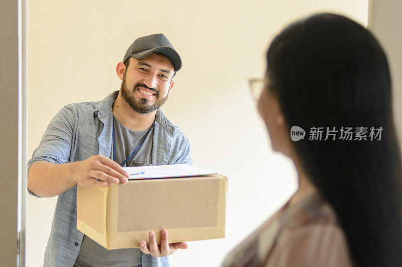 快递员在一个女人家门口给她送包裹。从家庭内部消费者的后视图