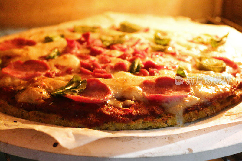 这是在烤箱里烤熟的自制花椰菜披萨，在披萨石上烤得薄而脆，上面放意大利辣香肠和新鲜的罗勒叶