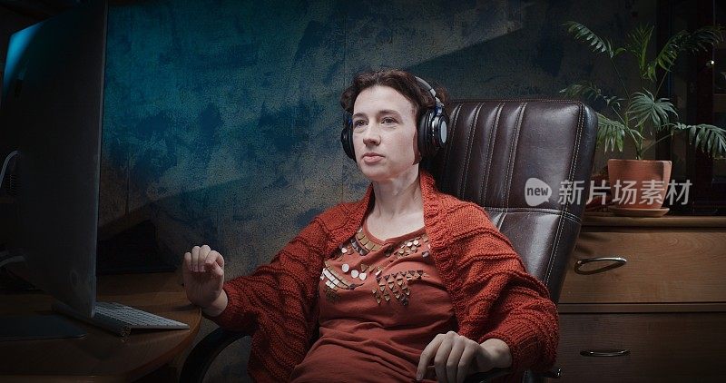一个在暗室里坐在电脑桌前使用耳机的成熟女人的翘臀肖像