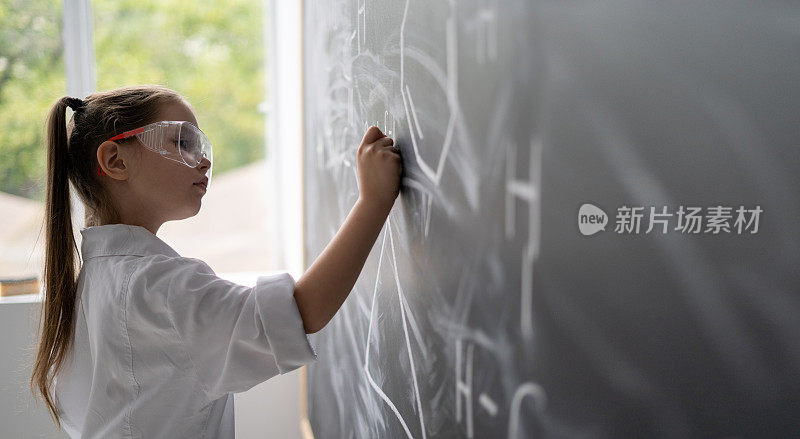 一个小女生在黑板旁解一道化学题。白色外套和护目镜。