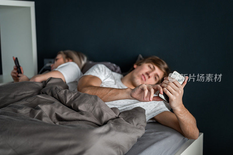 一对年轻夫妇躺在床上玩手机