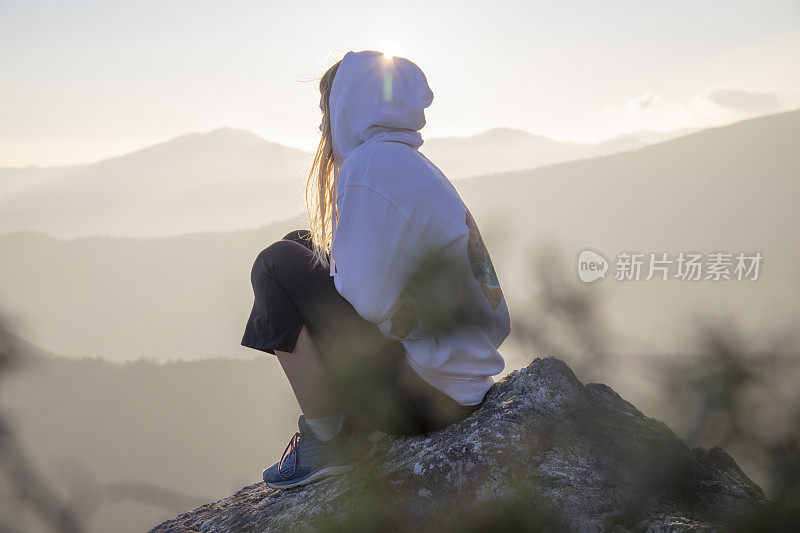 清晨，女徒步旅行者在阳光明媚的山脊上放松