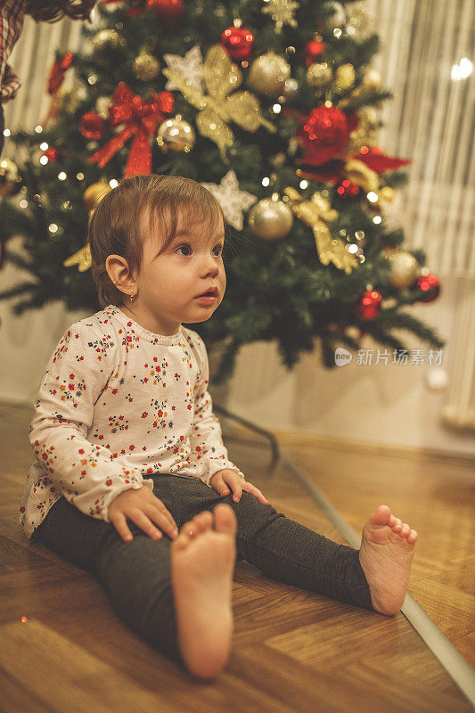 小女孩坐在装饰过的圣诞树前