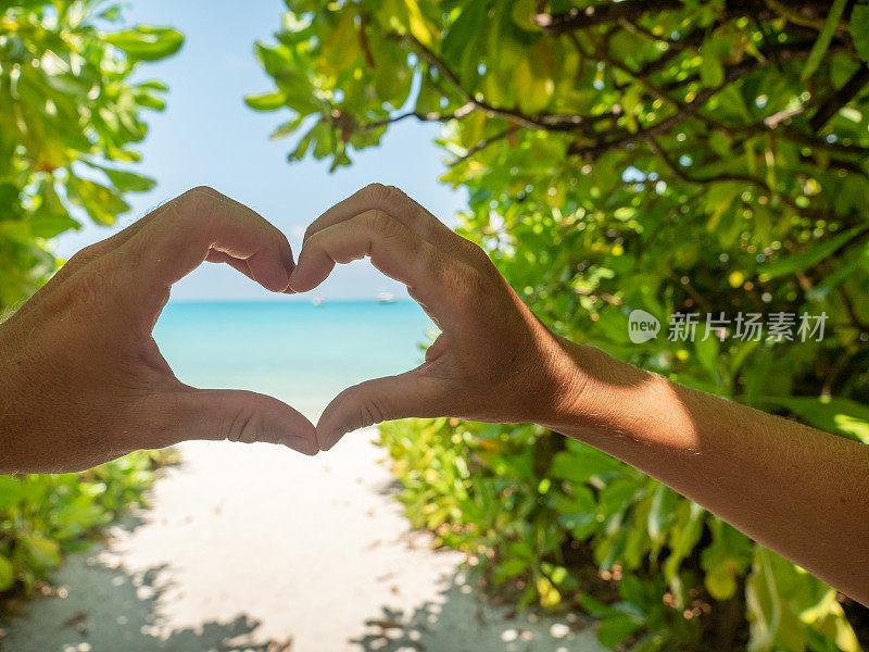 在日出的海滩上，一对夫妇用手做心的特写