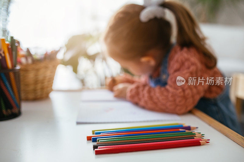 小女孩在家里学习，坐在课桌前，在学校的笔记本上写字