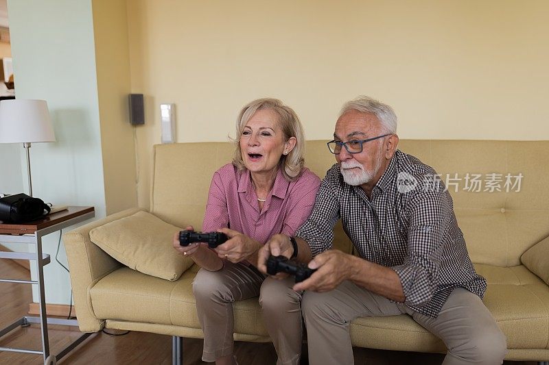 一位快乐的老妇人和她的丈夫在客厅玩电脑游戏。