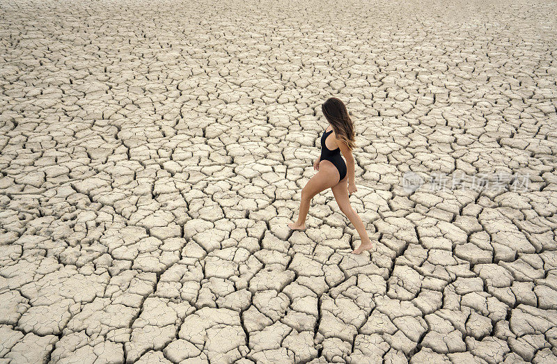 高角度的一个迷人的年轻女子站在开裂的干旱土地，干旱的概念