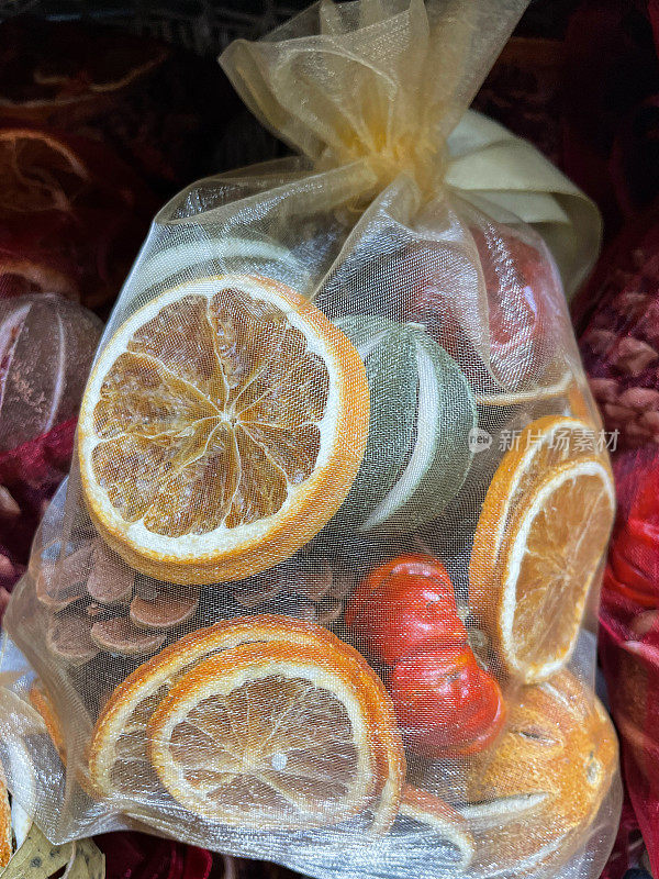 全帧图像的红色和黄色网袋含有干柑橘类水果(柠檬，酸橙和橘子)，松果和干月桂叶在柳条篮子，聚焦前景