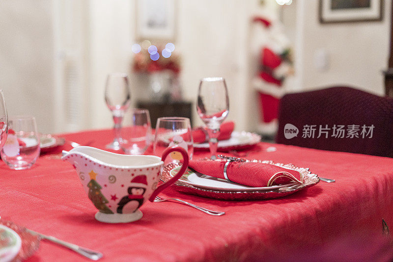 餐桌上铺着桌布和圣诞餐巾，还有盘子、玻璃杯和为庆祝活动准备的酱汁船