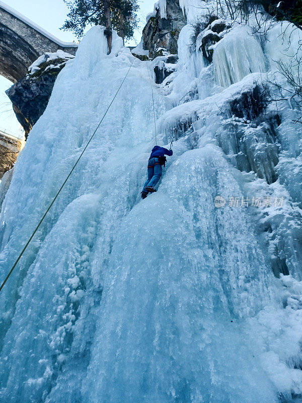 一个年轻人在冰冻的瀑布上攀冰，他使用冰镐