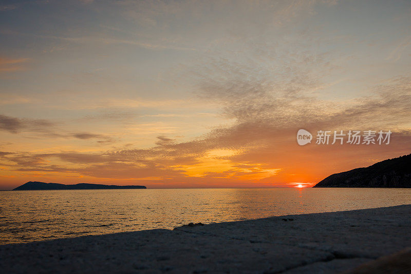日落景观，海与天空和一些云在海上，岛屿和一堵墙在前面，橙色的太阳在地平线上。Bisevo岛,克罗地亚