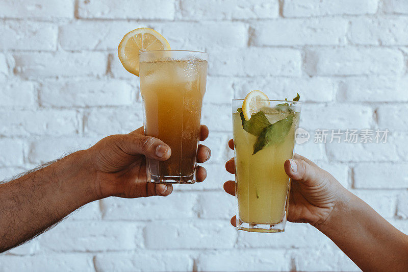 手拿柠檬水和冰茶在白色的背景，冷饮料在玻璃杯，薄荷柠檬水，冷茶柠檬