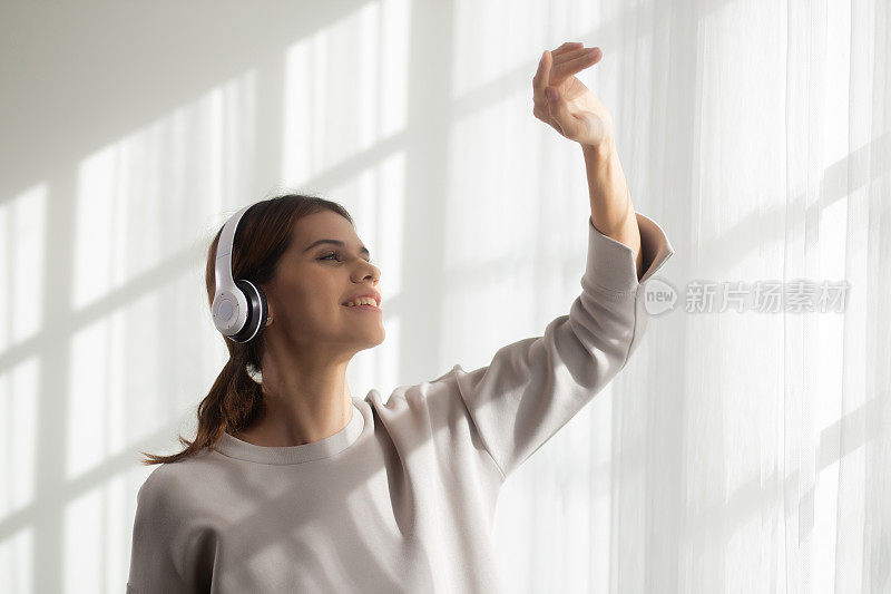 快乐女青年戴着耳机听着音乐边跳舞边唱歌，在客厅里尽情享受，快乐女青年带着娱乐，一个人，生活方式的理念。